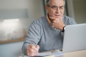 Senior Man At Home Connected On Laptop Computer researching Social Security Disability Insurance vs. Social Security Income