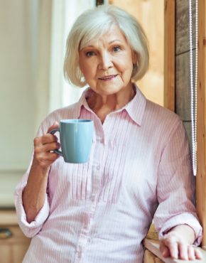 Smiling beautiful elder woman resting with hot drink at home researching long term care and social security benefits