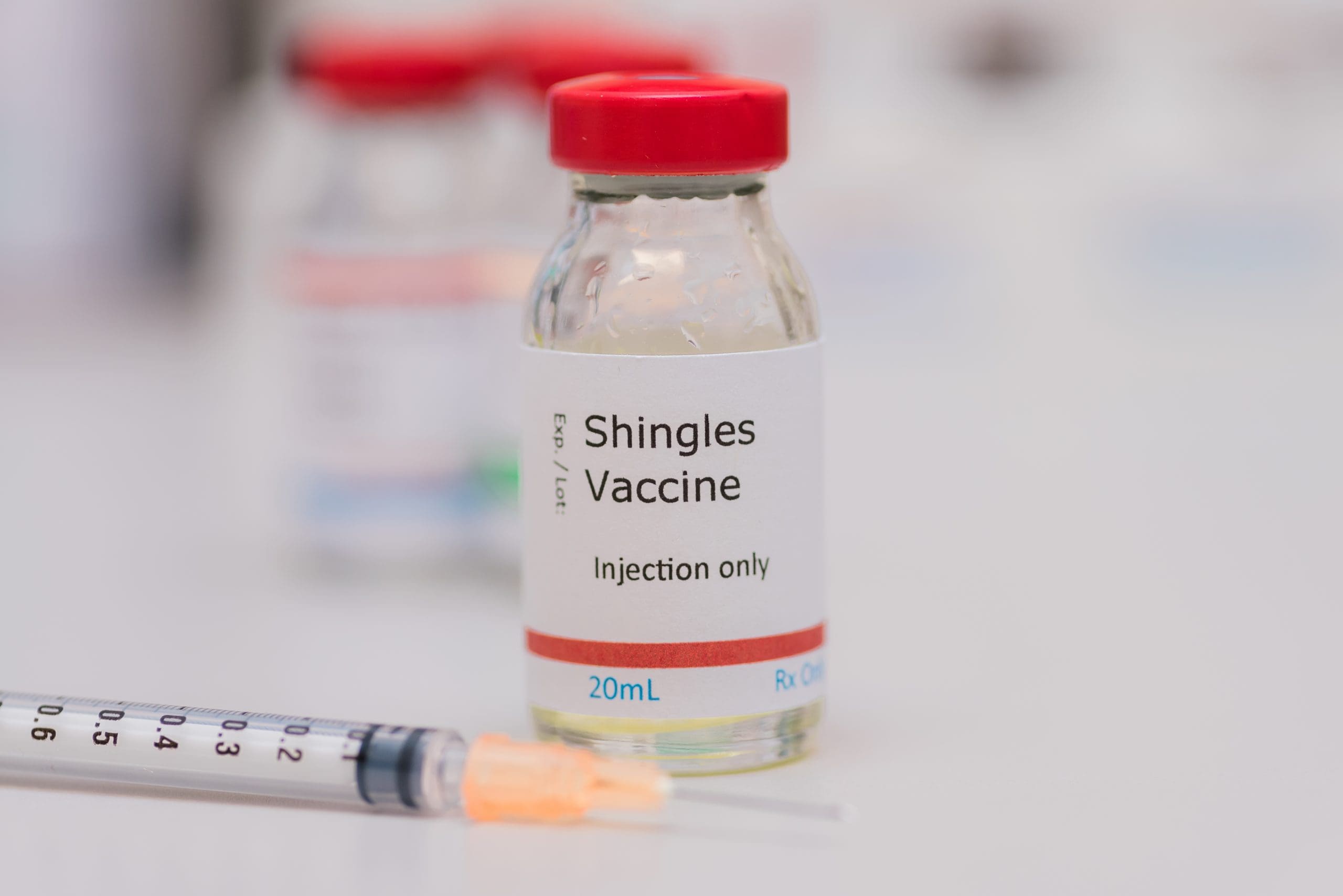 Shingles vaccine concept with syringe in foreground, vaccination vial on counter with additional vials in background