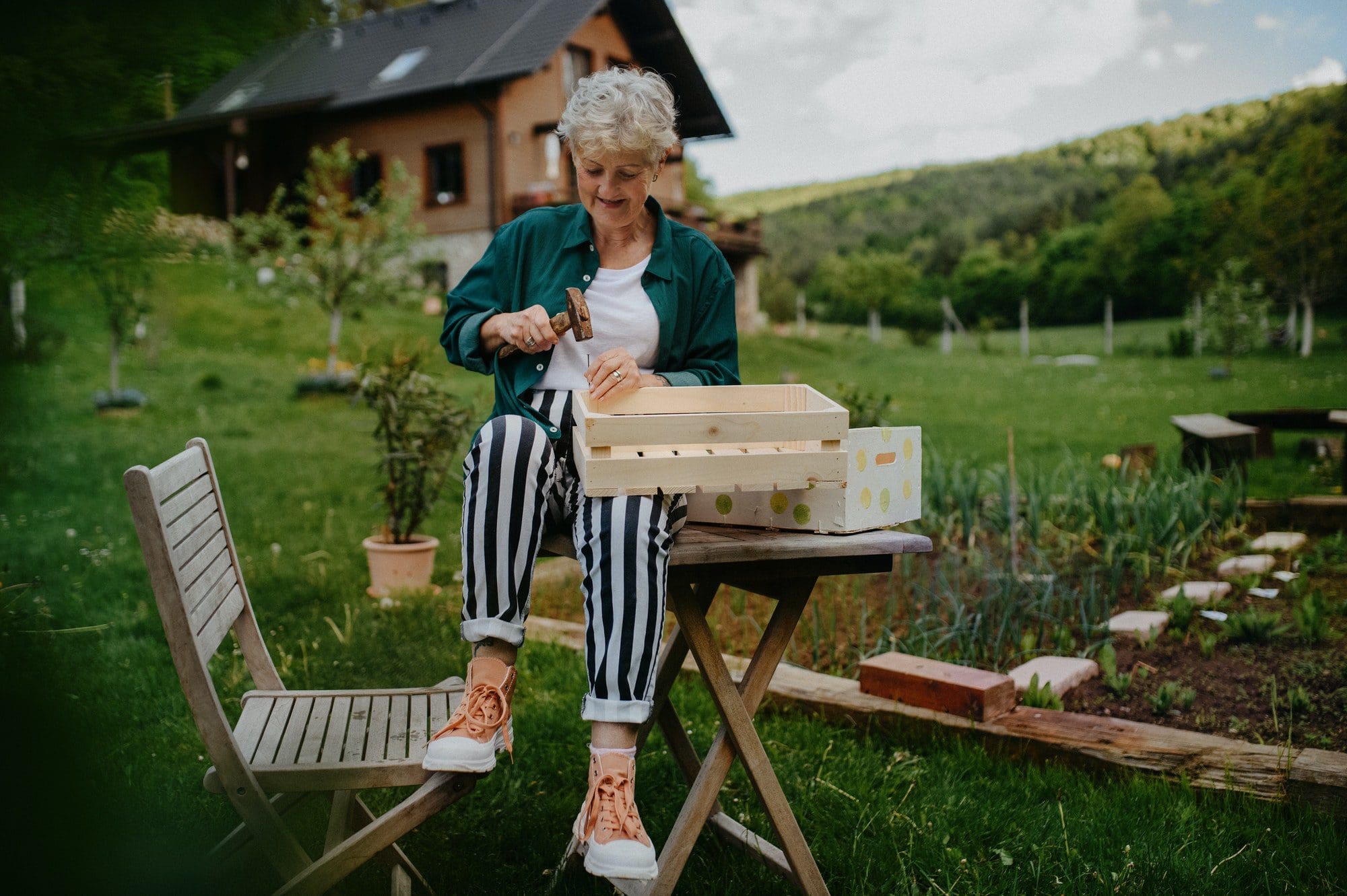 Happy senior woman renovating wooden crate outdoors in garden as she thinks over her Medigap Plan I.